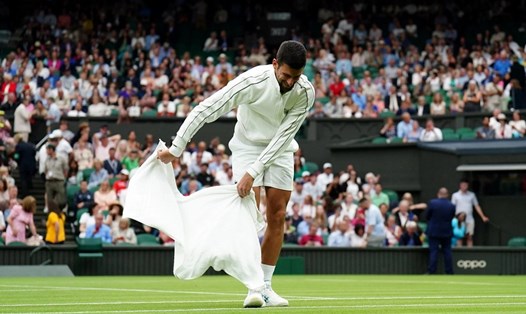 Novak Djokovic dùng khăn thấm mặt cỏ sân Trung tâm. Ảnh: Wimbledon