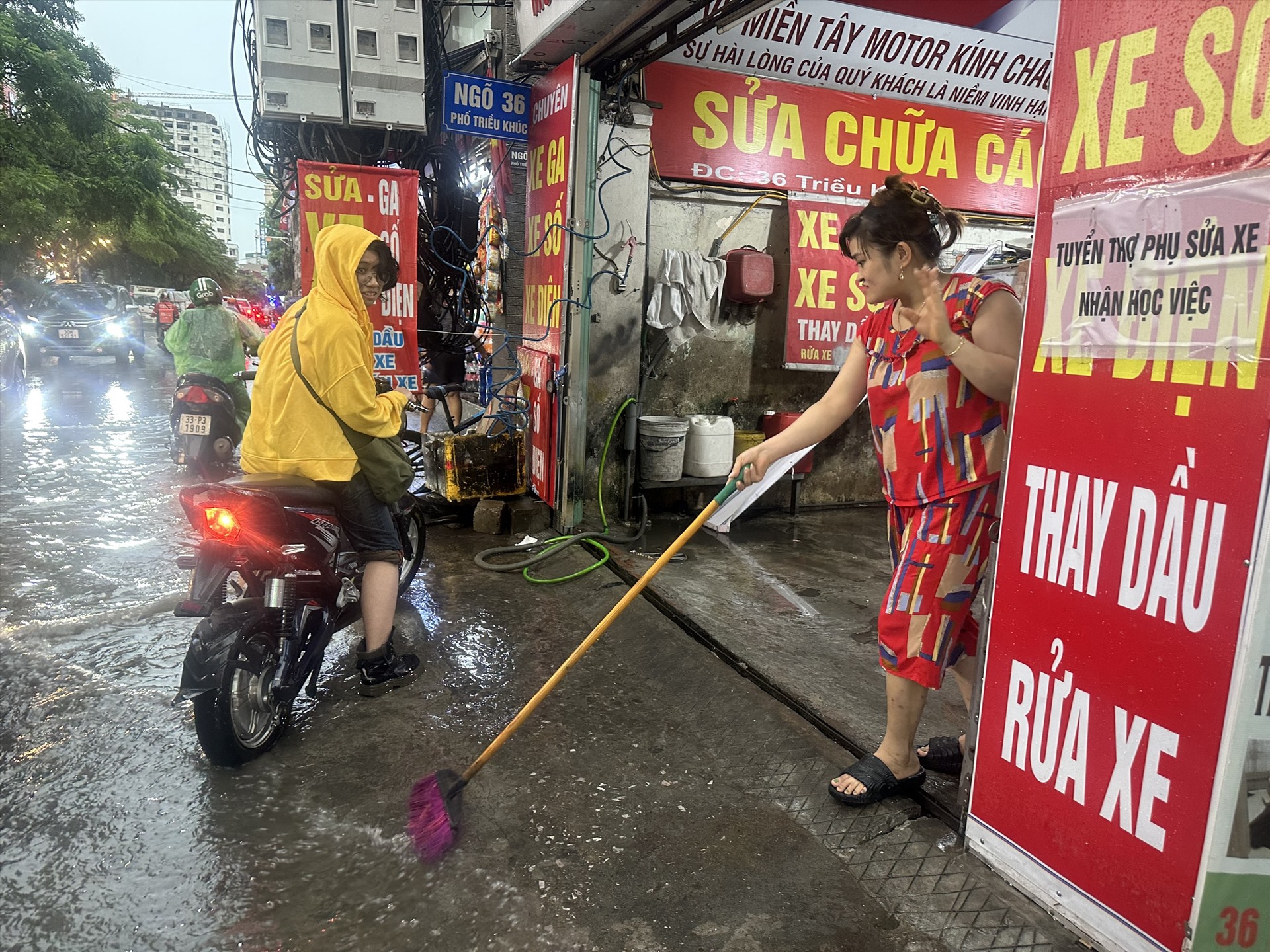 Chủ quán sửa xe máy tại 36 Triều Khúc liên tục dùng chổi hắt nước để tránh nước ngập vào cửa hàng.  