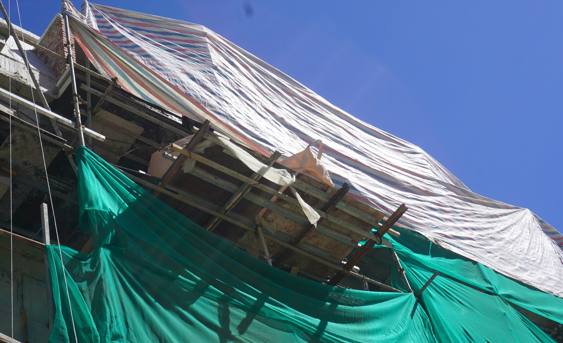 Trên tầng cao của các ngôi nhà, công nhân phải căng những tấm bạt che nắng để làm việc. Ảnh: Quách Du
