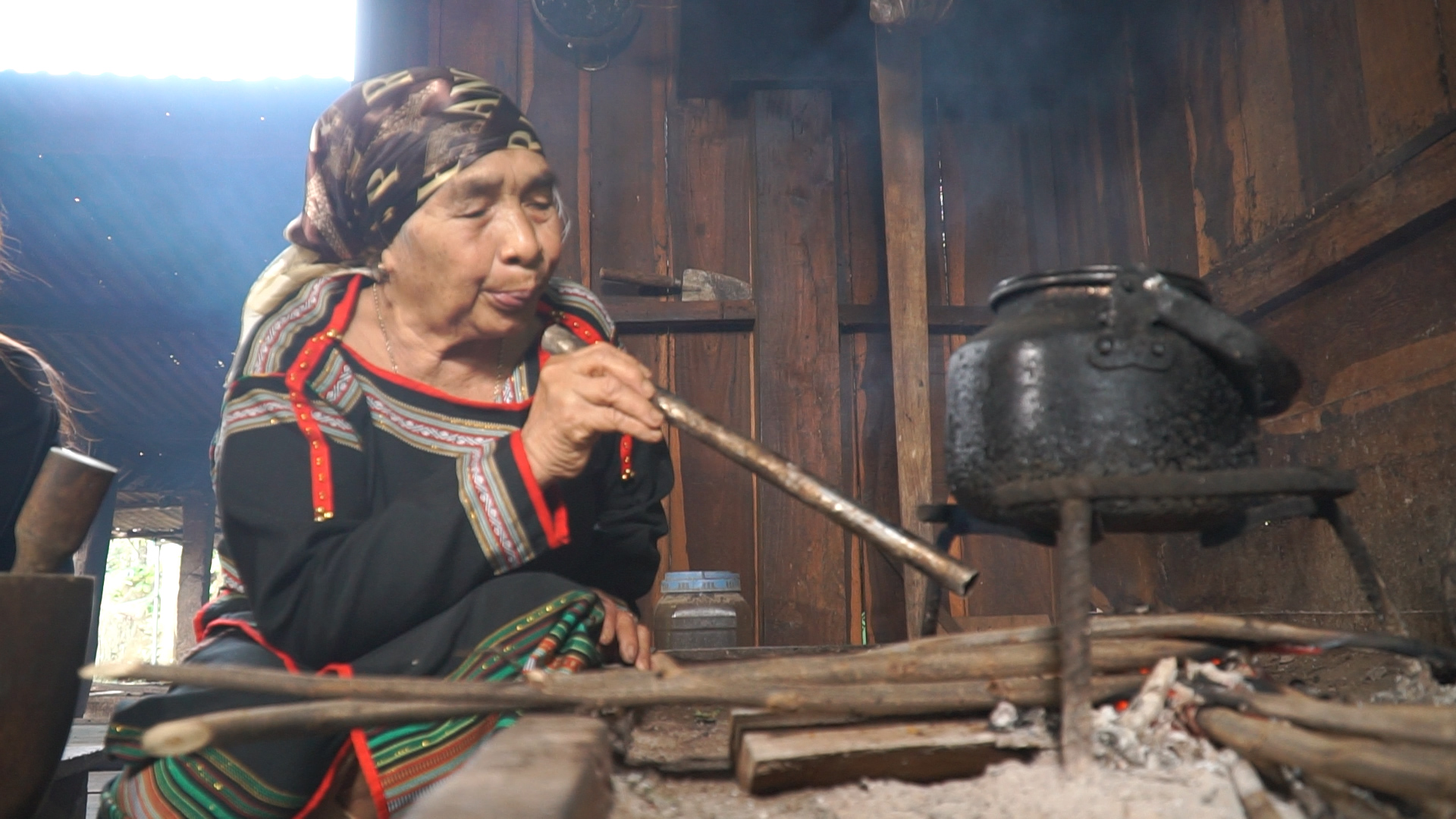 Một cụ bà người đồng bào dân tộc Ê Đê thổi lửa ở bếp nhà dài truyền thống. Ảnh: Bảo Trung