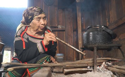 Một cụ bà người đồng bào dân tộc Ê Đê thổi lửa ở bếp nhà dài truyền thống. Ảnh: Bảo Trung