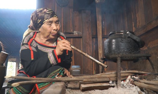 Một cụ bà người đồng bào dân tộc Ê Đê thổi lửa ở bếp nhà dài truyền thống. Ảnh: Bảo Trung