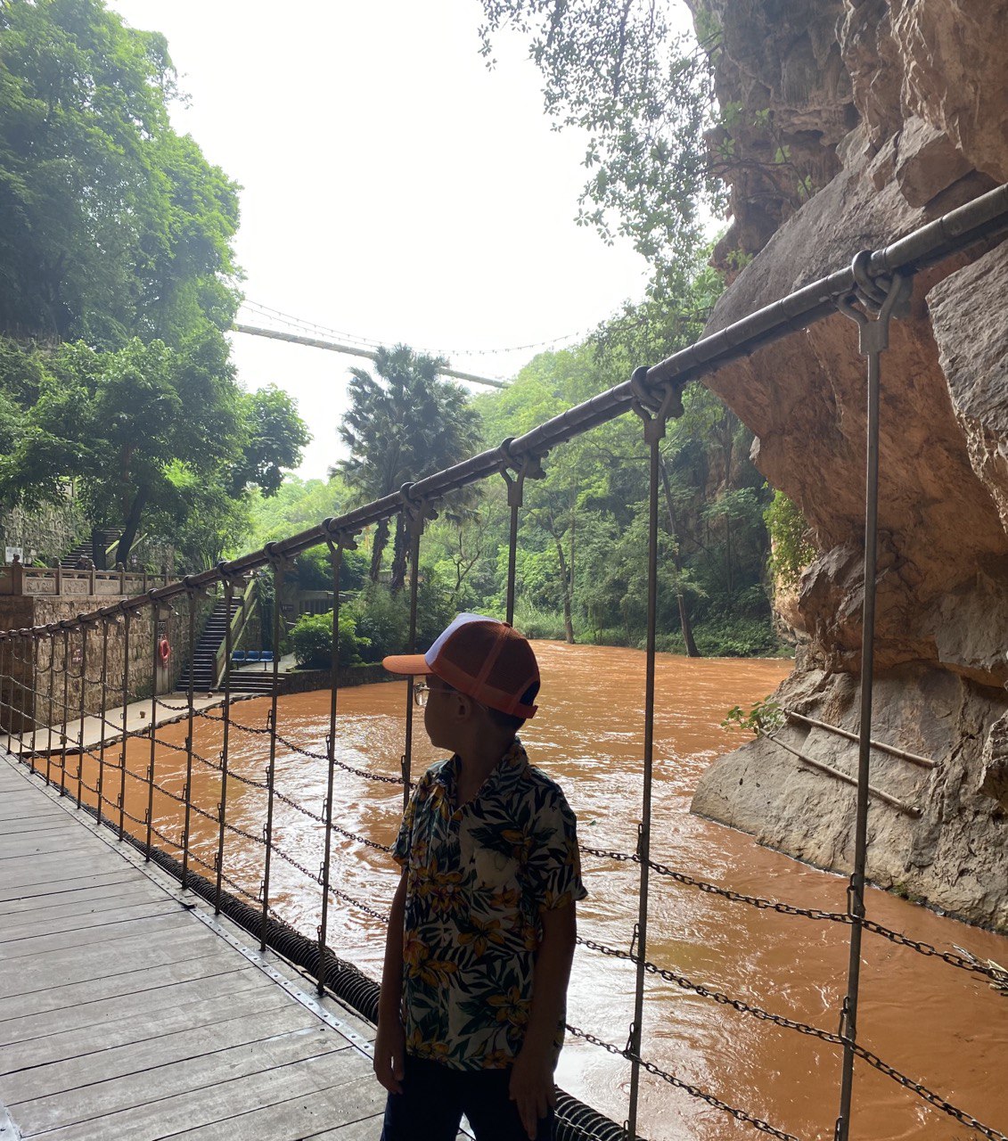 Du khách băng qua một cây cầu dây gỗ, tiến vào hành lang lát đá đi sâu vào trong động. Bên dưới cây cầu là dòng sông Hồng chảy xiết.