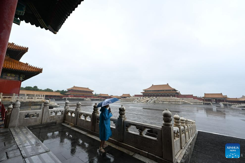 Một nhà báo tác nghiệp dưới trời mưa bên trong Tử Cấm Thành ngày 31.7.2023. Ảnh: Xinhua