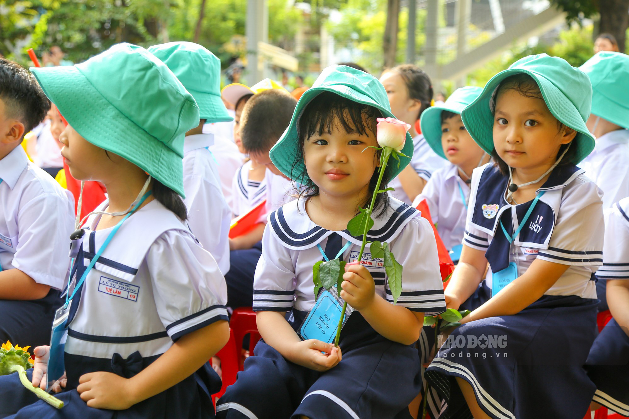 Các em học sinh lớp 1 được cầm hoa, cầm cờ với vẻ mặt rạng ngời trong ngày khai giảng ở ngôi trường mới.