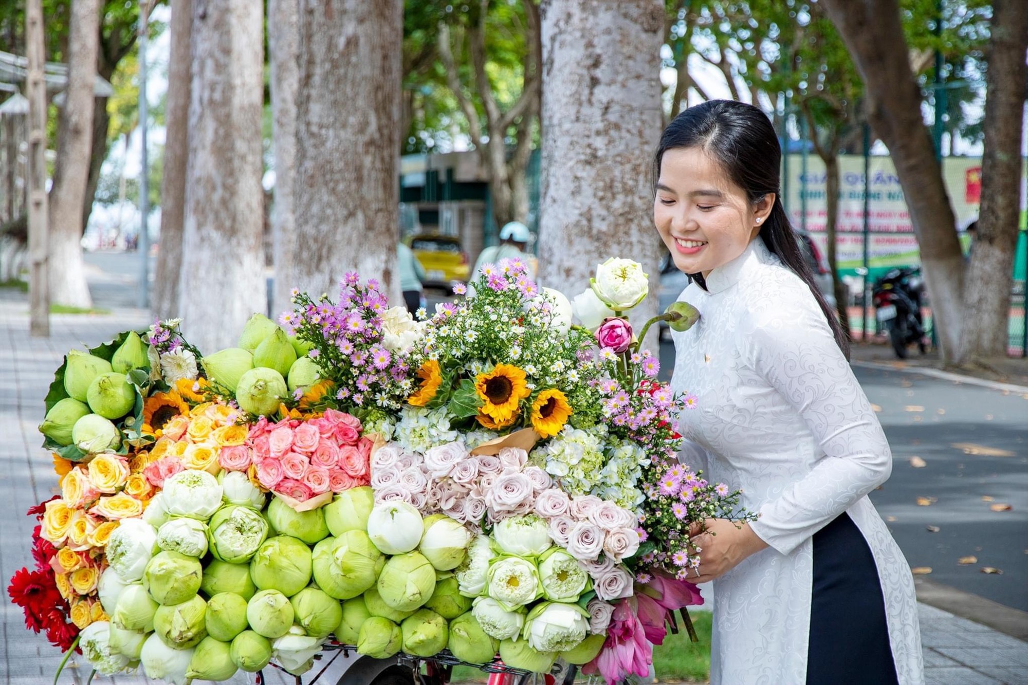 Thiếu nữ trong trang phục áo dài dịu dàng tạo dáng bên xe chở đầy hoa ở bờ hồ Nguyễn Du. Ảnh: Kim Luận