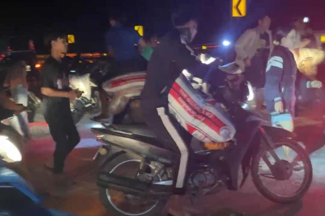 Một người dùng xe môtô chở các bao gạo nếp lấy từ xe ôtô tải bị lật. Ảnh: Tạo Nguyễn.