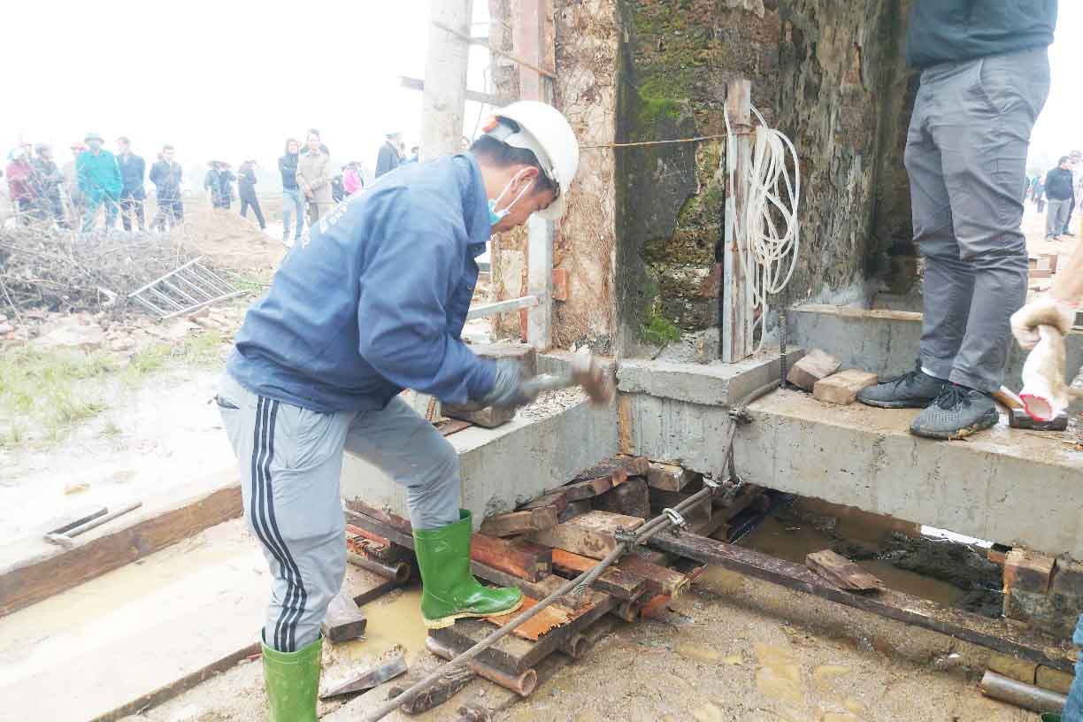 Công nhân của Công ty TNHH xử lý lún nghiêng Nguyễn Văn Cư đang chèn các con lăn để di dời cổng đền. Ảnh: Trần Tuấn.