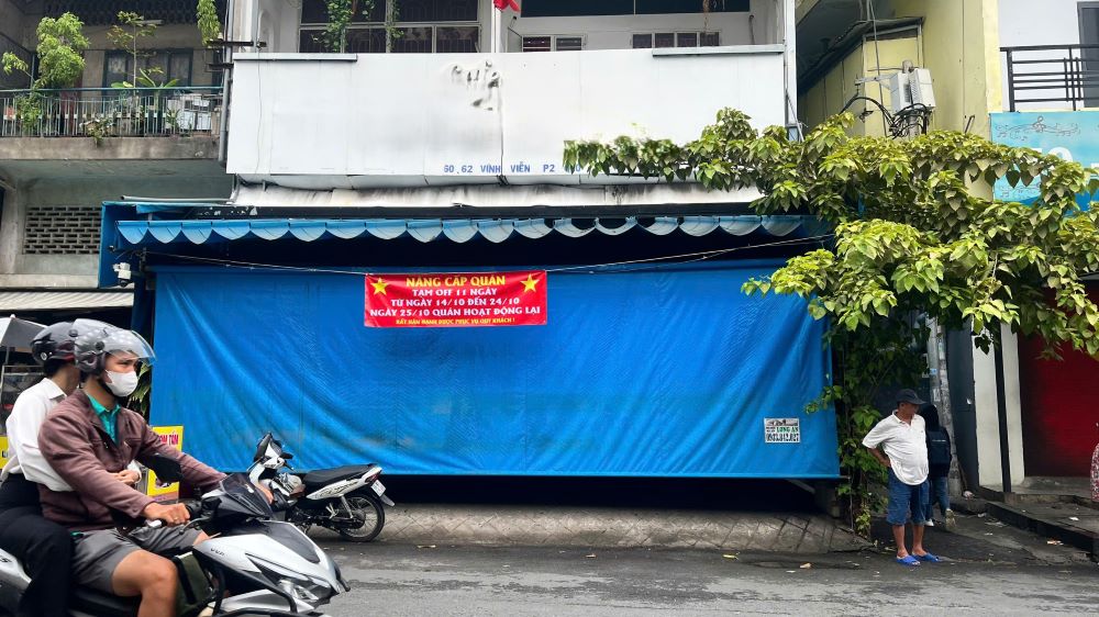 Hiện trường – nơi xảy ra vụ vợ chồng chủ quán cà phê tử vong trên đường Vĩnh Viễn (Quận 10, TPHCM) đang che kín bạt xanh phía trước quán. 