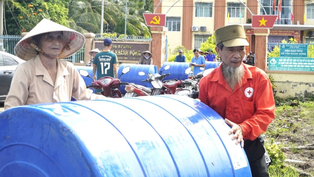 Can bo Hoi Chu thap do ho tro nguoi lon tuoi, di lai kho khan dem bon chua nuoc ve nha. Anh: Nguyen Anh