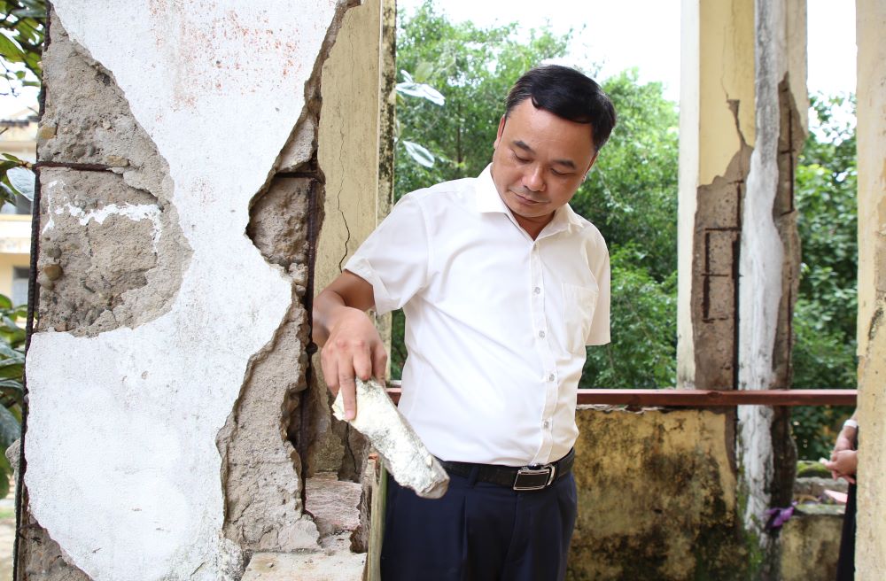 The principal of Vinh Linh Boarding Ethnic High School next to a wall that is no longer intact.