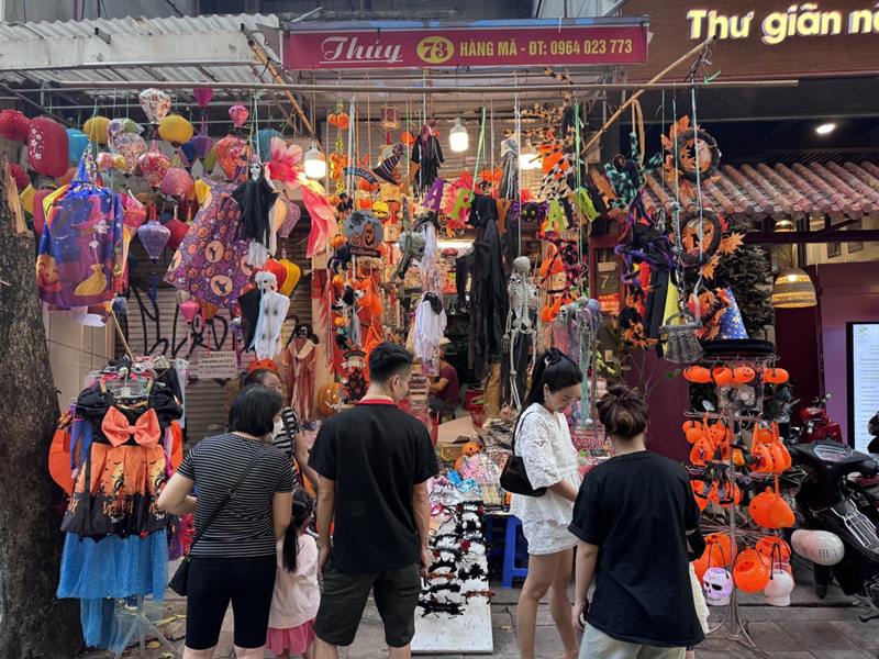 Ngay Halloween can ke, cac cua hang tren pho Hang Ma (Hoan Kiem, Ha Noi) phu kin sac mau ruc ro cua muon van do trang tri tu lon nho, voi tong mau chu dao la cam, den va trang. Nam nao tuyen pho cung thu hut dong dao gioi tre va cac gia dinh nho tai Ha Noi den check-in, mua sam phuc vu le hoi Halloween.