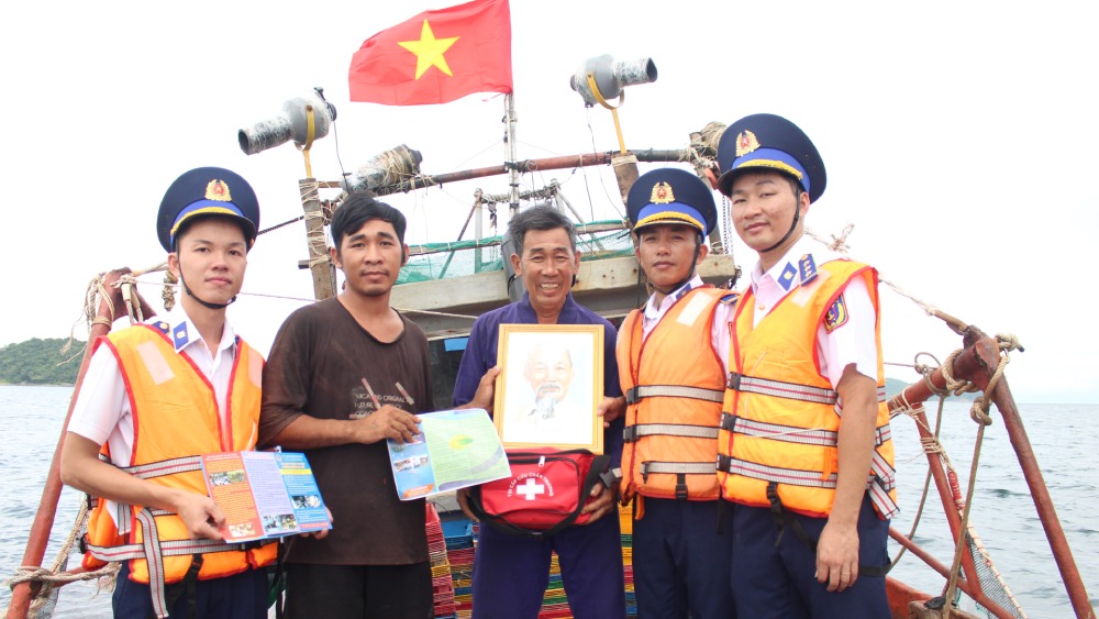 Cán bộ BTL Vùng Cảnh sát biển 4 tặng ảnh Bác Hồ, túi thuốc y tế và phát tờ rơi tuyên truyền cho ngư dân. Ảnh: BTL vùng CSB4