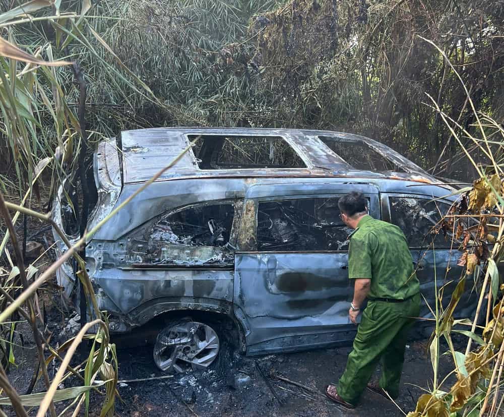 Police examine the burned-out car, leaving only the frame. Photo: Lam Hong