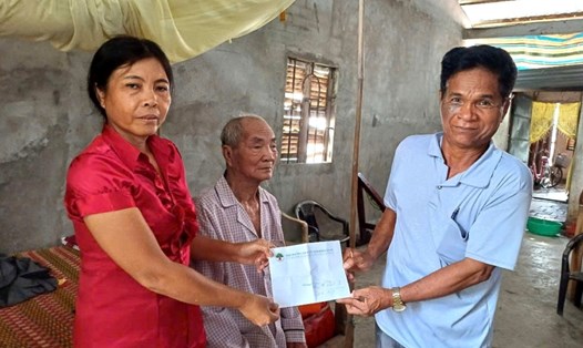 Ông Danh Hương (gần 100 tuổi, đồng bào dân tộc Khmer) được ông Lâm hỗ trợ và hướng dẫn làm thủ tục nhận trợ cấp. Ảnh: Xuân Nhi