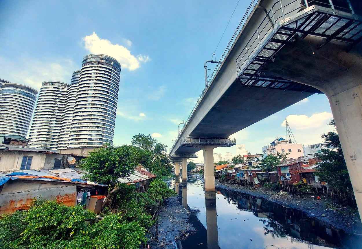 A row of dilapidated houses along Van Thanh canal, next to high-rise buildings and the elevated section of Metro No. 1 running through. Photo: MINH QUAN