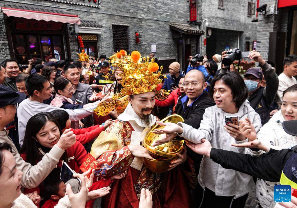 Một nhân viên trong trang phục Thần Tài giao lưu với khách du lịch ở Nam Ninh, Khu tự trị dân tộc Choang Quảng Tây, Trung Quốc, ngày 14.2.2024. Ảnh: Xinhua