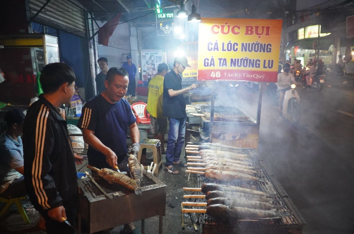 Từ khoảng 20h, nhưng cửa hàng bán cá lóc nướng trên đường Tân Kỳ Tân Quý (quận Tân Phú, TPHCM) đã tất bật chuẩn bị từ việc làm rau, nhóm lửa, làm cá, nướng chín... để kịp sáng sớm có cá phục vụ người dân vào ngày vía Thần tài.