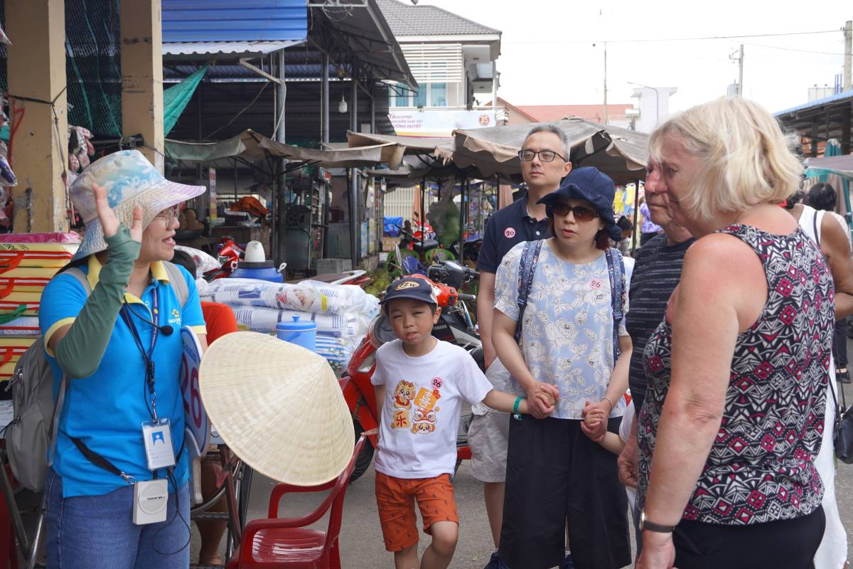 Du khách quốc tế được giới thiệu về nón lá Việt Nam tại chợ Hòa Long. Ảnh: Thành An