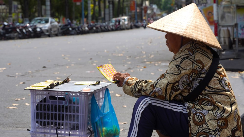 Ngồi bán vé số giữa tiết trời oi bức tại khu vực Bến Ninh Kiều, bà Nguyễn Thị Kim Hương (63 tuổi) với khuôn mặt khắc khổ, mồ hôi nhễ nhại trên làn da nhăn nheo, cầm xấp vé số mời người đi đường để kiếm từng đồng lẻ.