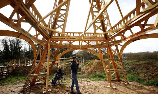 Hai thợ mộc đang làm việc với bản sao tháp Eiffel bằng gỗ. Ảnh: Chụp màn hình