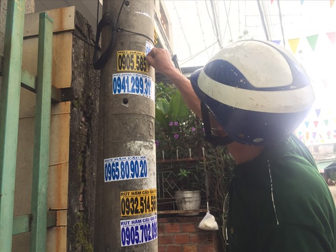 Người dân Đà Nẵng tự gỡ bỏ các số điện thoại quảng cáo ở trước nhà mình. Ảnh: Nguyễn Linh