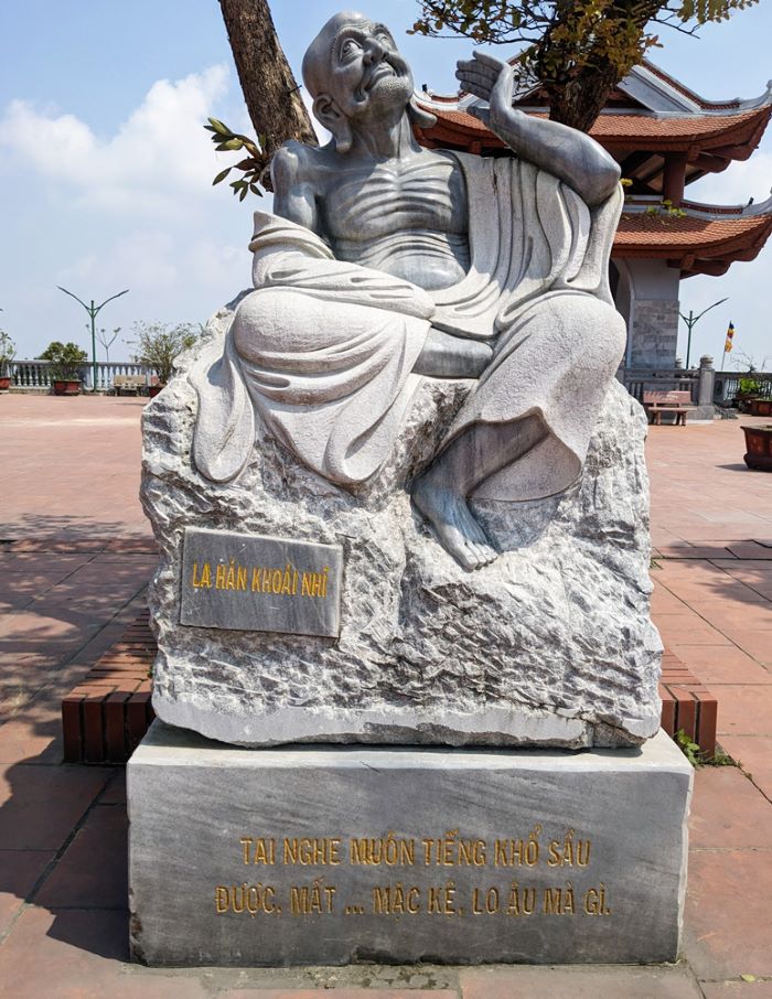 Phía dưới bức tượng tạc vị La Hán Khoái Nhĩ có hai câu đề khắc lên đá: “Tai nghe muôn tiếng khổ sầu/ Được mất… mặc kệ, lo âu mà gì”. Ảnh: Huyền Linh
