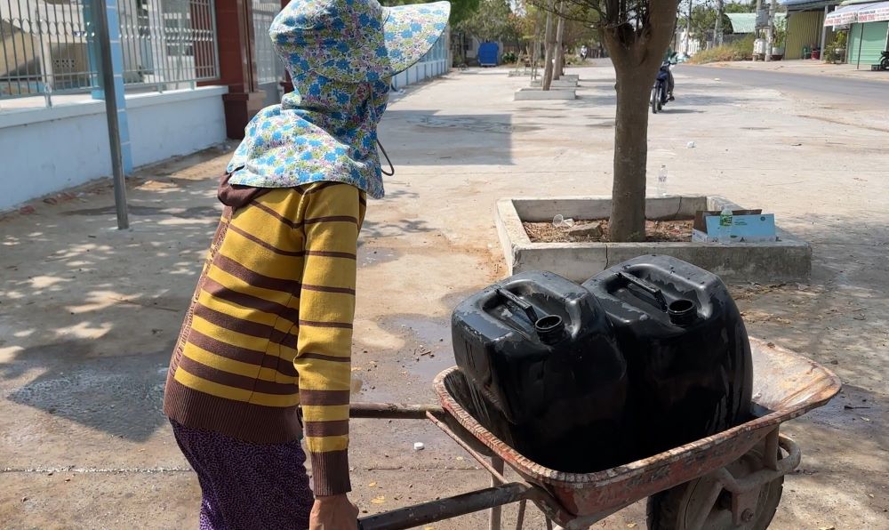 Bà Nguyễn Thị Minh cố đẩy chiếc xe rùa chở 2 thùng nhựa đựng nước về dùng. Ảnh: Duy Tuấn