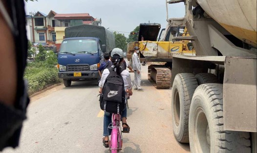 Xe tải đi vào đường làng đúng giờ tan học, khiến nhiều em học sinh vất vả di chuyển. Ảnh: Vân Trường