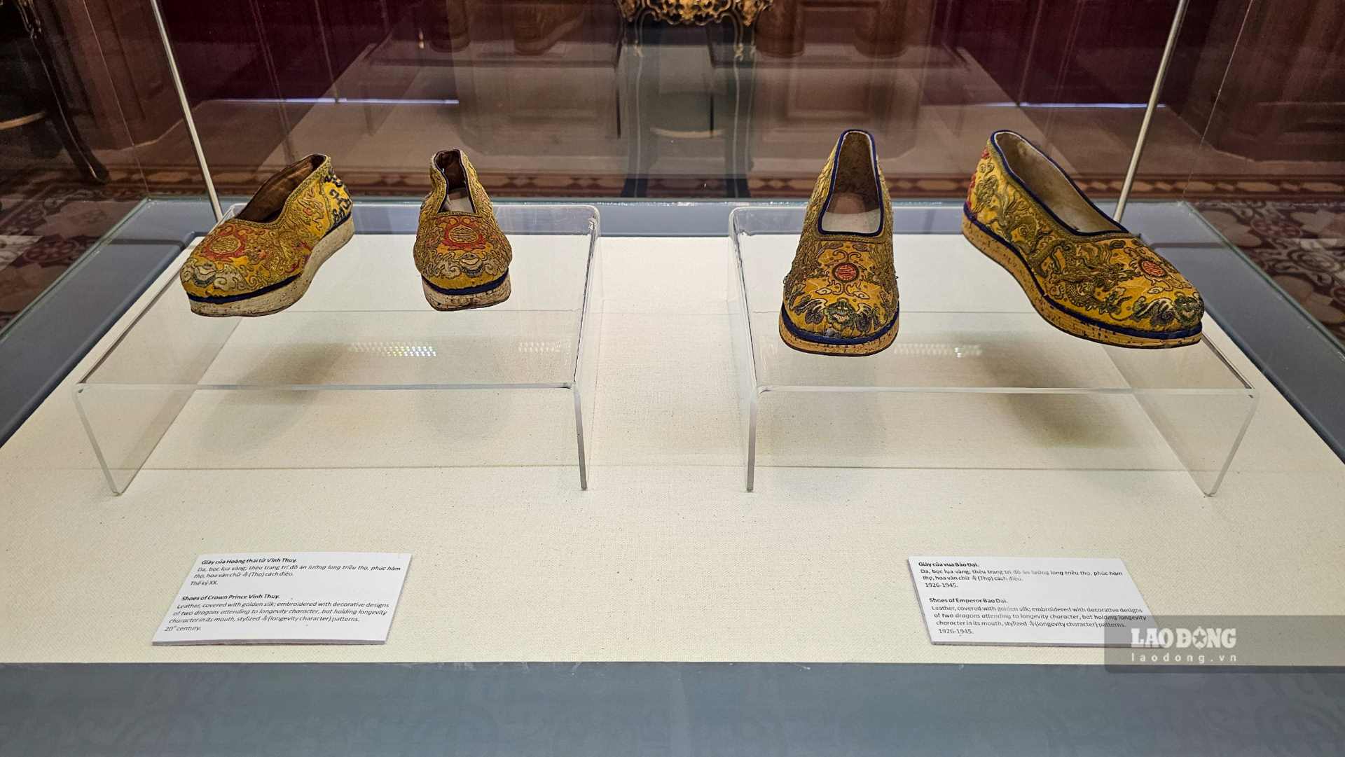 Giày của vua Bảo Đại (phải) và giày của Hoàng thái tử Vĩnh Thụy (trái) được làm từ da, bọc lụa vàng, thêu trang trí đồ án lưỡng long triều thọ, phúc hàm thọ, hoa văn chữ (Thọ) cách điệu. 
