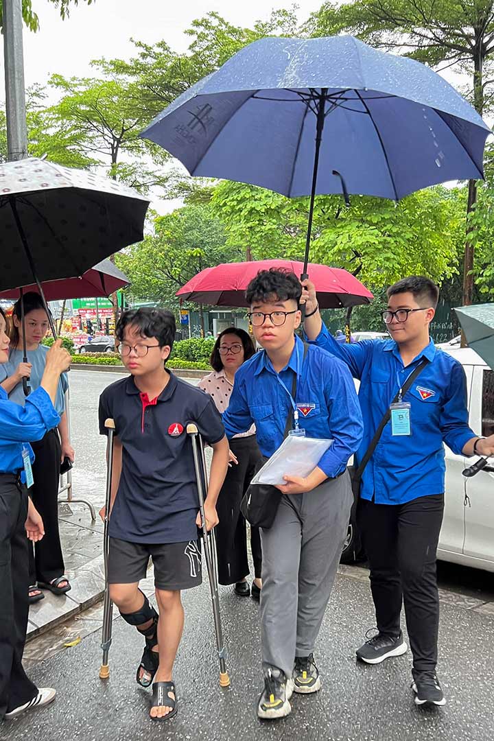 Thí sinh chống nạng được hỗ trợ đưa vào phòng thi tại điểm thi Trường THCS Yên Hoà (Cầu Giấy).