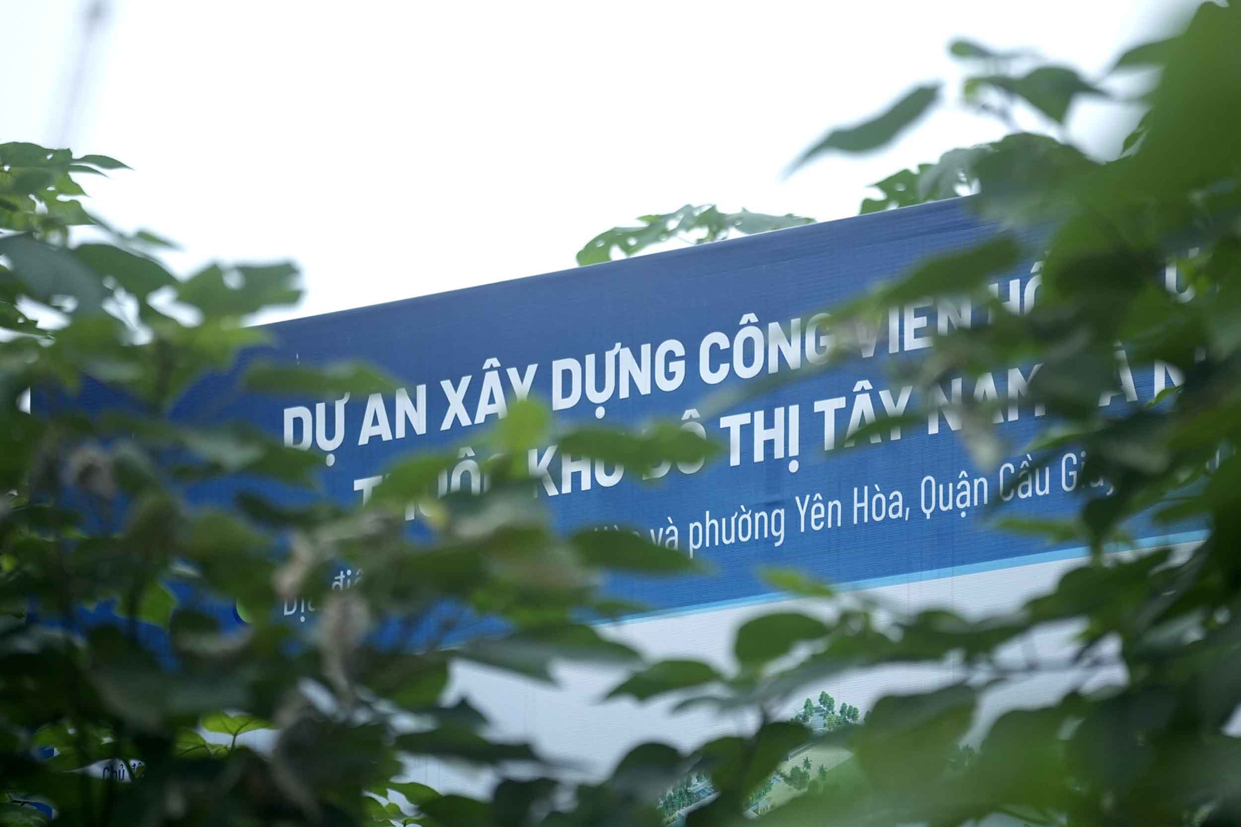 Tấm biển “dự án xây dựng công viên hồ điều hòa thuộc khu đô thị Tây Nam Hà Nội” nằm ở ngã tư phố Nguyễn Chánh - Mạc Thái Tông bị cây xanh che khuất.