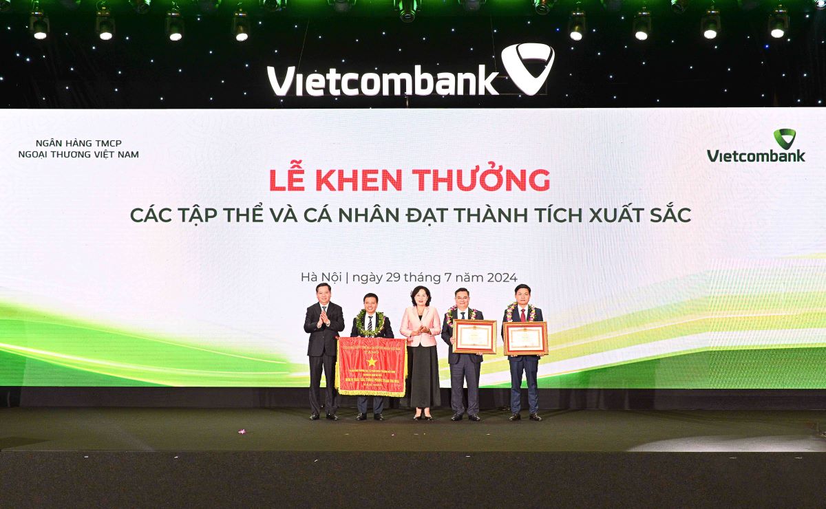 Comrade Nguyen Thi Hong - Member of the Party Central Committee, Governor of the State Bank of Vietnam (center) along with Comrade Nguyen Long Hai - Alternate Member of the Party Central Committee, Secretary of the Party Committee of the Central Business Bloc (far left) presenting the Flag, Certificate of Merit, and flowers to congratulate the collectives and individuals honored to receive the Government's Emulation Flag and the Prime Minister's Certificate of Merit. Photo: Vietcombank.