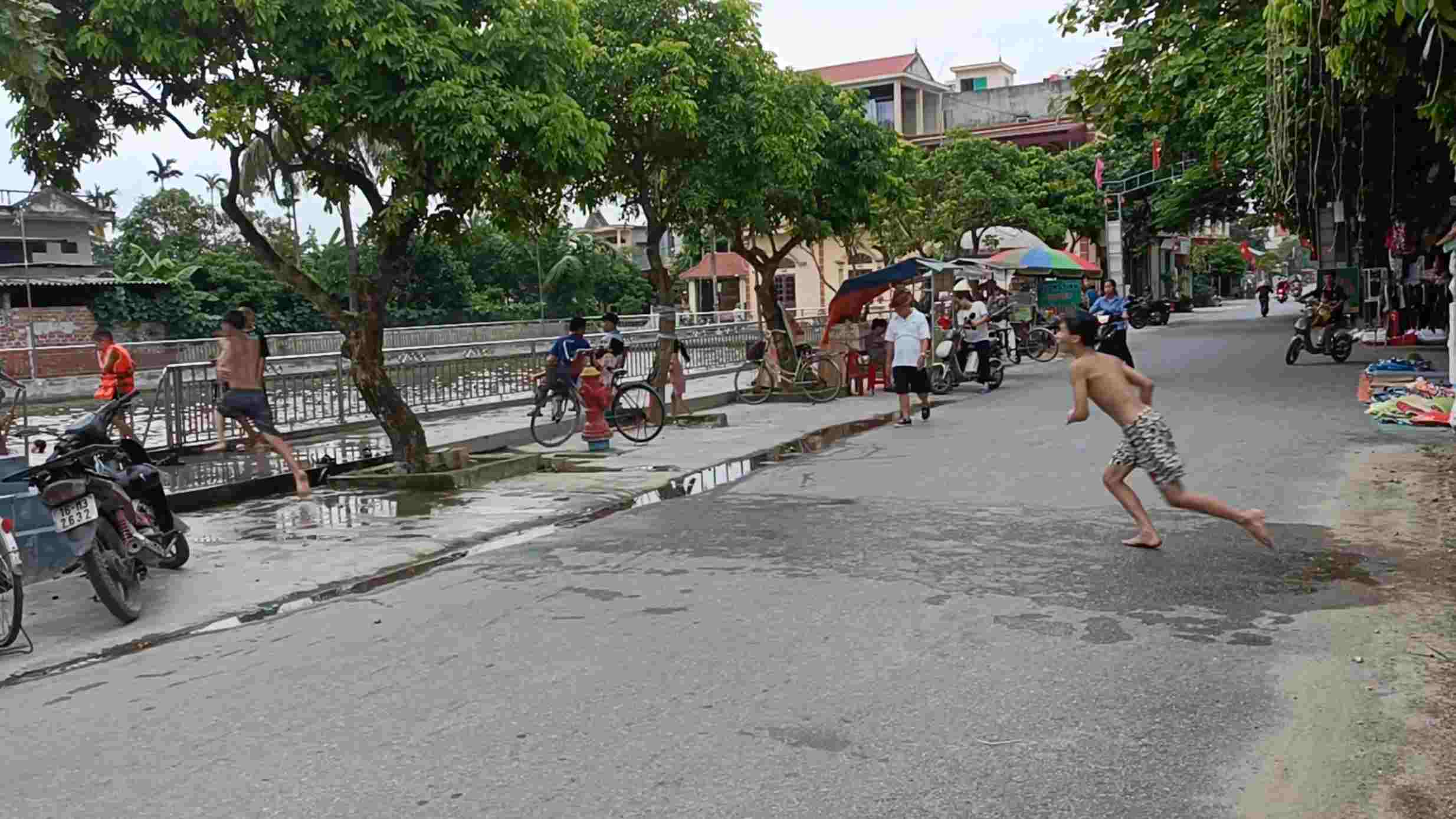 Nhiều em nhỏ còn chạy băng qua đường để lấy đà nhảy xuống hồ bơi, gây nguy hiểm cho người tham gia giao thông. Ảnh: Hoàng Khôi