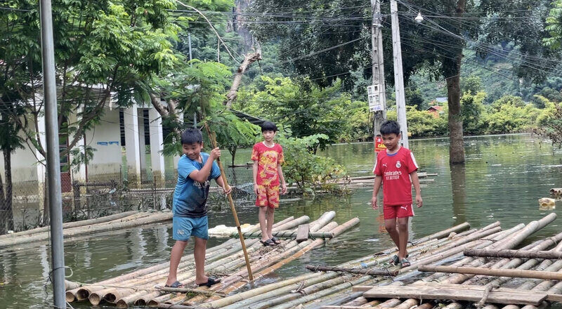 Nước lũ dâng cao, người dân phải sử dụng bè tre để di chuyển, tiềm ẩn nhiều nguy hiểm cho trẻ em. Ảnh: Khánh Linh