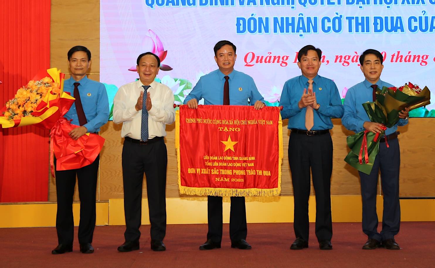 Phó Bí thư Thường trực Tỉnh ủy, Chủ tịch HĐND tỉnh Quảng Bình Trần Hải Châu và Phó Chủ tịch Tổng LĐLĐ Việt Nam Nguyễn Xuân Hùng trao Cờ thi đua của Chính phủ và tặng hoa chúc mừng LĐLĐ Quảng Bình. Ảnh: Công Sáng