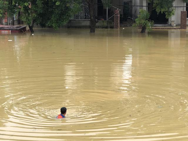 A resident swims through the water from a flooded residential area to get out.