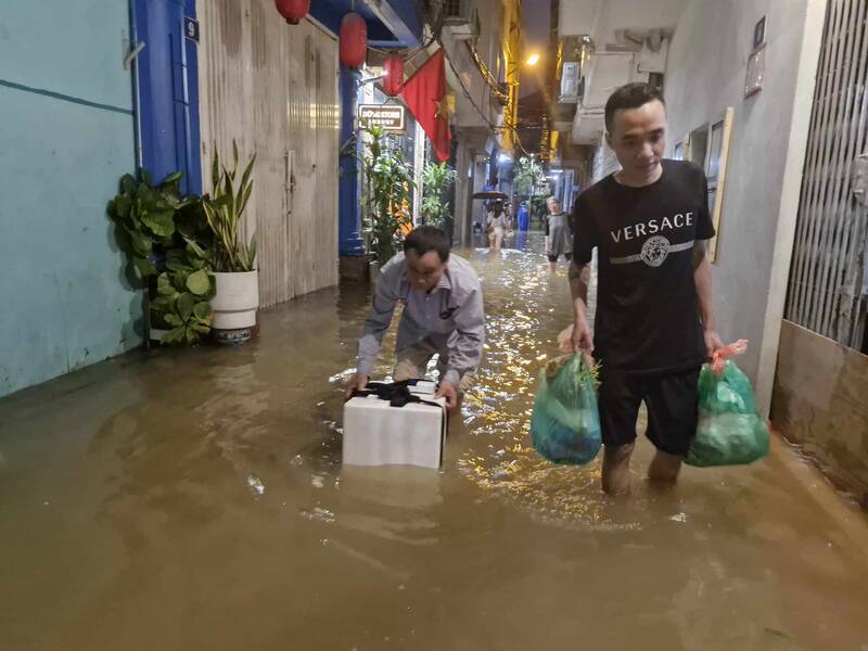 Anh Đồng Xuân Quân (bên phải, sinh năm 1995, phường Chương Dương, quận Hoàn Kiếm) xách đồ đạc, nhu yếu phẩm chạy lụt trong đêm 10.9. Ảnh: Thu Giang