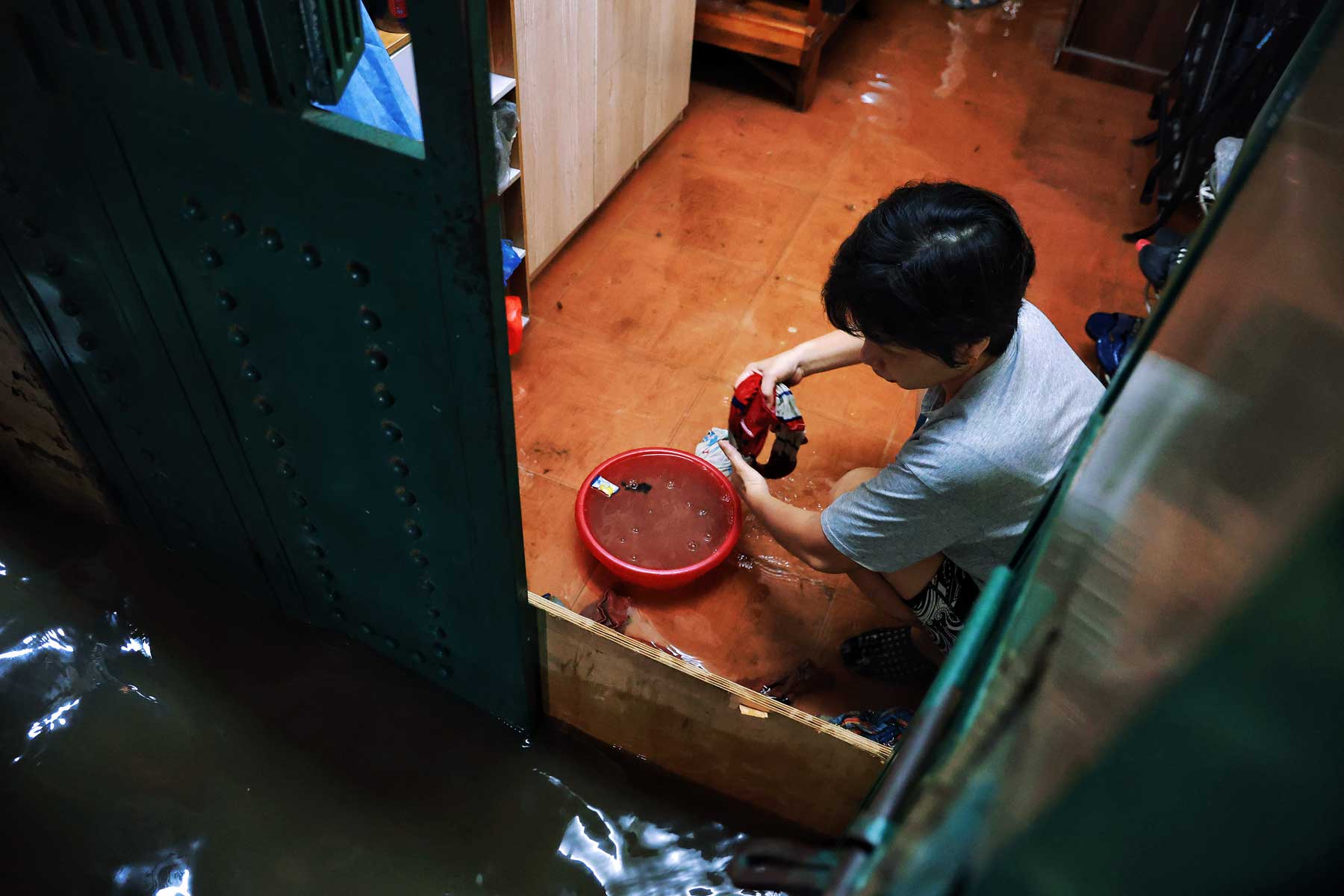 Nước ngập tràn vào nhà nên người phụ nữ này phải lấy khăn để thấm nước, đồng thời, chỉ cũng phải dùng ván để chắn ngang cửa, phòng rác trôi vào nhà.