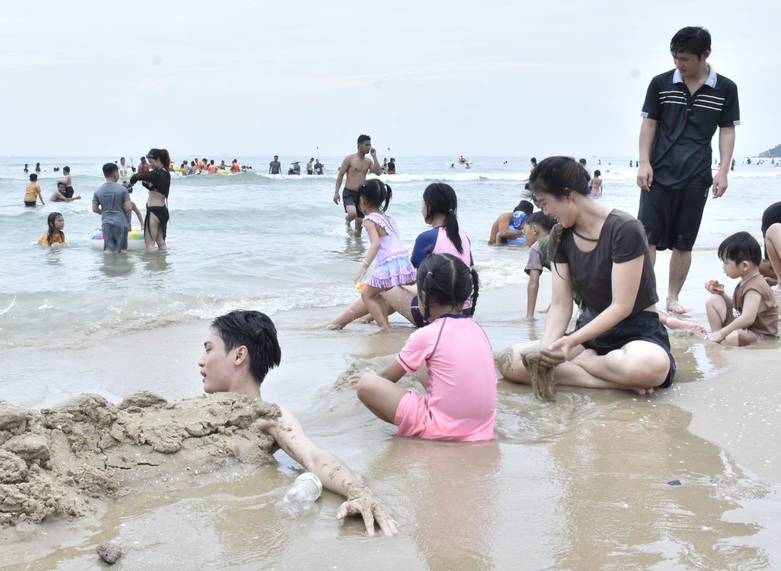 Chị Hoài Thương (áo đen, ngồi) vui chơi cùng gia đình trên bãi biển. Ảnh: Thành An