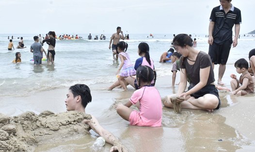 Chị Hoài Thương (áo đen, ngồi) vui chơi cùng gia đình trên bãi biển. Ảnh: Thành An