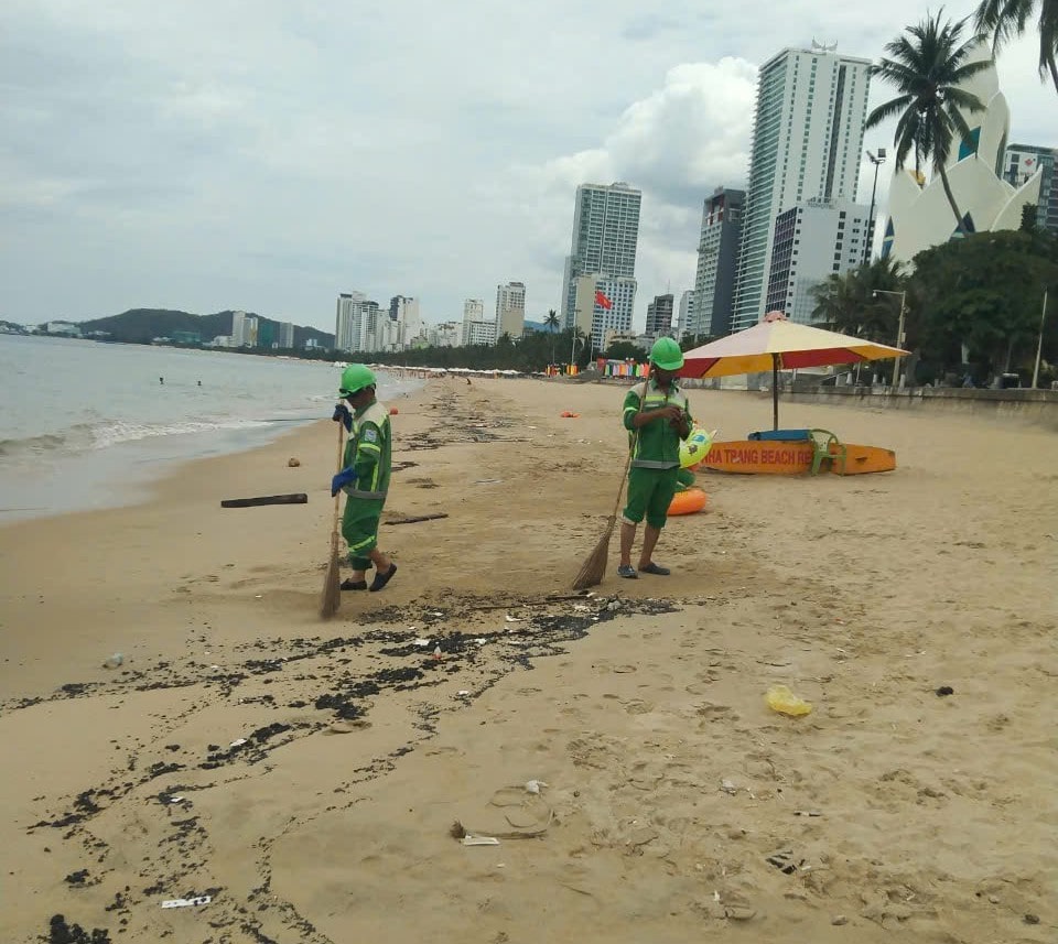 Nhân viên Công ty CP môi trường Đô thị Nha Trang thu dọn dầu vón cục dạt vào bờ biển. Ảnh: Hữu Long