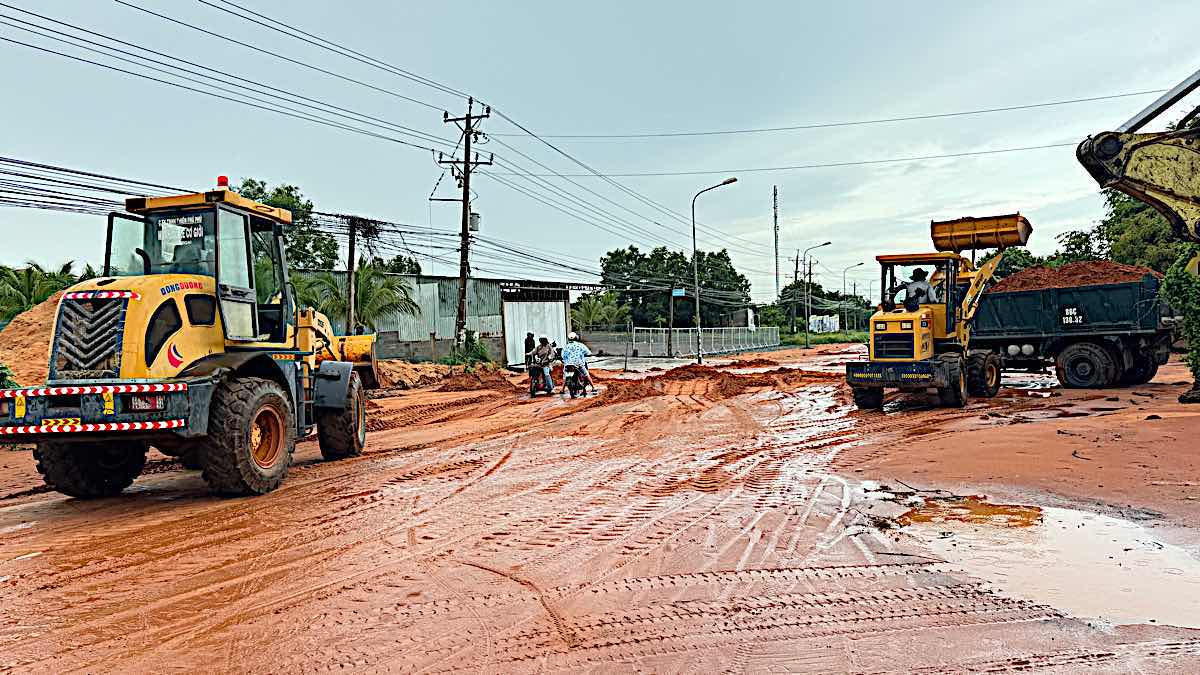 Xe múc cào cát đỏ trên mặt đường để xe ben chở đi. Ảnh: Duy Tuấn 