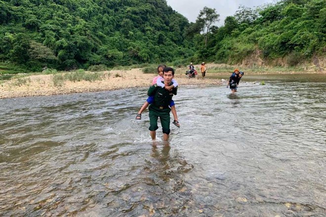 Cán bộ biên phòng cõng bé gái lội qua suối để đảm bảo an toàn, kịp dự lễ khai giảng năm học mới. Ảnh: P.Vĩnh