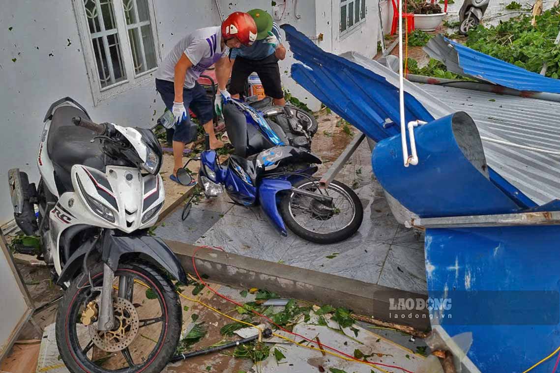 Anh Vũ Văn Khánh (áo xanh) đang cùng người nhà lật mái tôn để đưa những chiếc xe máy bị mắc kẹt ra ngoài. Gia đình anh Khánh là một trong những hộ dân kinh doanh dịch vụ ăn uống, nhà nghỉ bị thiệt hại nặng nề sau bão. Anh ước tính thiệt hại hơn 3 tỉ đồng.