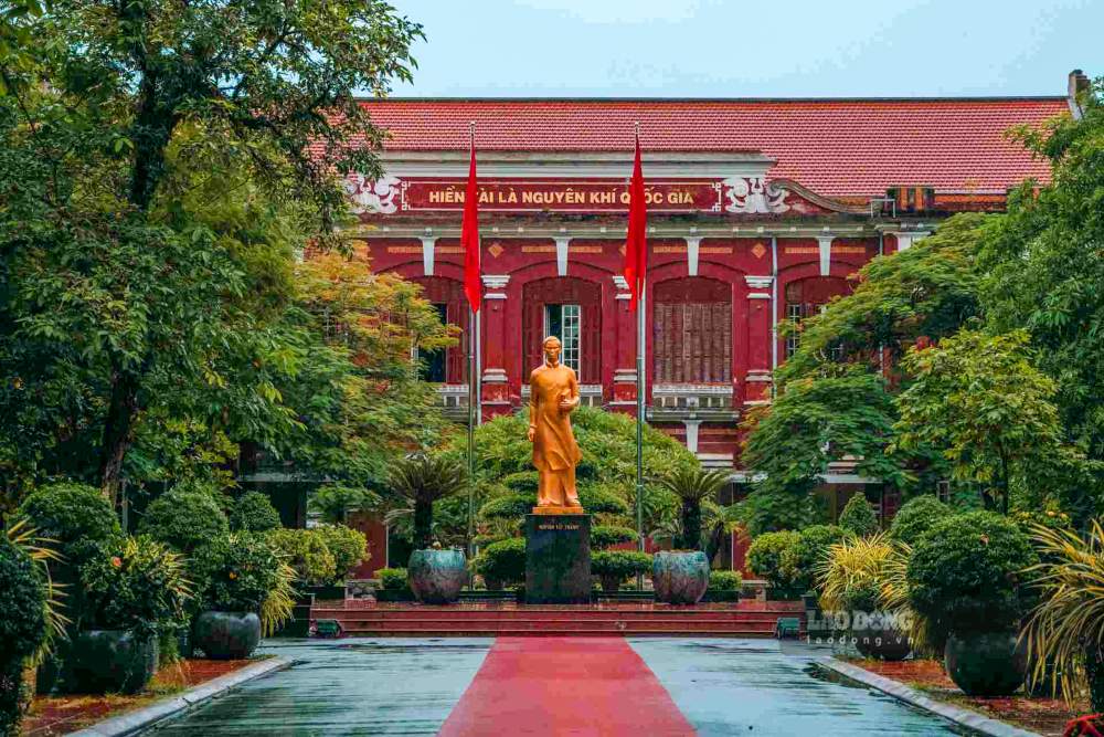 Tuong “cuu hoc sinh Nguyen Ai Quoc” dat trang trong giua san truong. Phia sau la day lop hoc co co in dong chu vang noi tieng: “Hien tai la nguyen khi Quoc gia”.