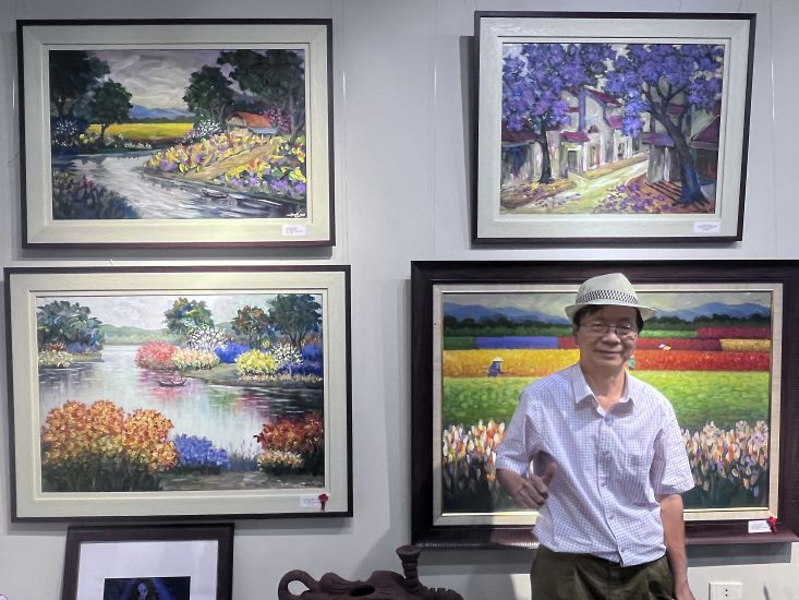 Teacher, painter Nguyen Huu Hanh and some of his many paintings at the exhibition. Photo: Viet Van