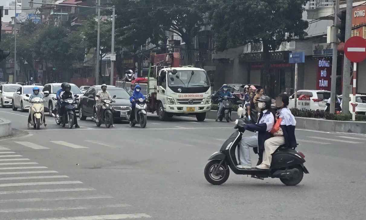 A female student drove an electric motorbike carrying a rear-seated person participating in traffic without a helmet. Photo: Nguyen Truong