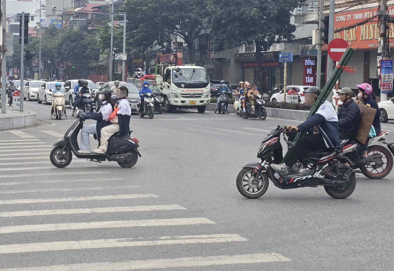 Mot hoc sinh dieu khien xe dap dien cho theo nguoi ngoi sau khong doi mu bao hiem. Anh: Nguyen Truong