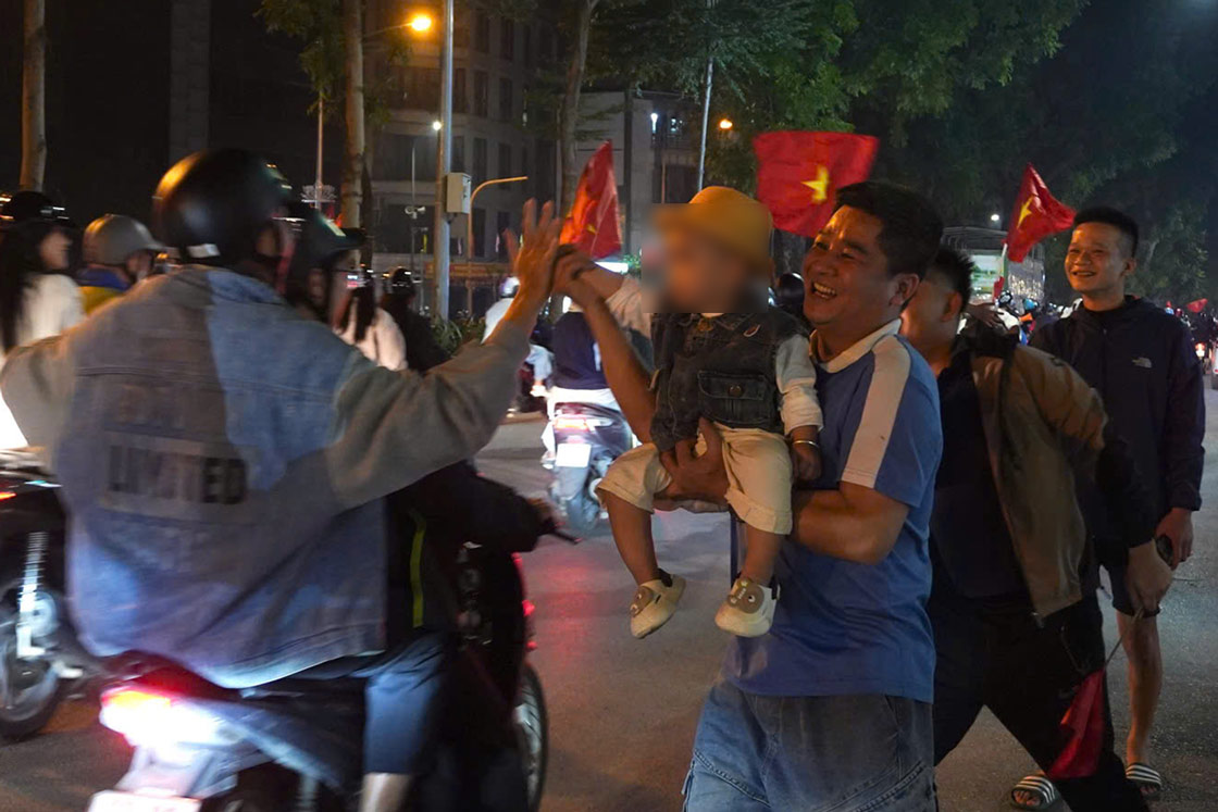 Anh Vu Thanh Cong (Ha Noi) be theo con nho hoa vao dong nguoi an mung chien thang, guong mat rang ro giua rung co do sao vang. Trong tieng coi xe va tieng ho reo vang khap pho phuong, anh chu dong dung lai bat tay, dap tay chuc mung nhung nguoi xa la cung chung niem vui. Anh: Trang Anh - Huyen Trang